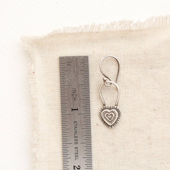 A layered heart earring next to a ruler for size reference