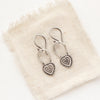 The layered heart earrings styled on tan linen