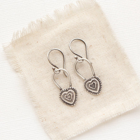 The layered heart earrings styled on tan linen