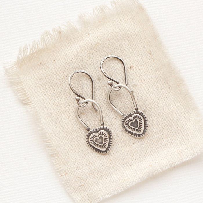 The layered heart earrings styled on tan linen