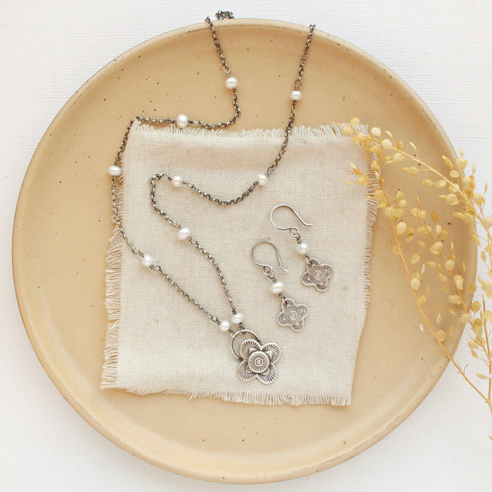 The layered talara pearl necklace styled with the matching mini talara pearl earrings on a tan plate with linen and dried grass