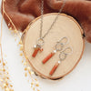 The canyon sydney charm necklace and matching earrings styled on wood with orange velvet and dried grass.