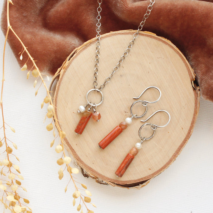 The canyon sydney charm necklace and matching earrings styled on wood with orange velvet and dried grass.