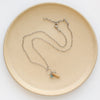 The oasis sydney charm necklace styled on a tan plate to show the adjustable lobster clasp closure.
