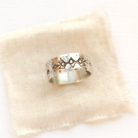 A rustic stamped silver ring styled on tan linen