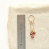 A garnet trio gold hoop earring next to a ruler for size reference