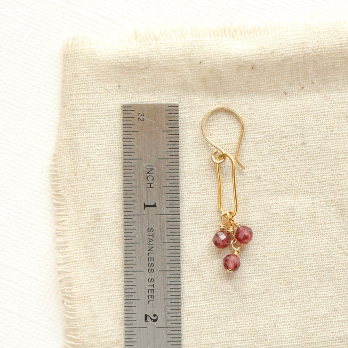 A garnet trio gold hoop earring next to a ruler for size reference