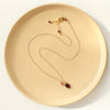 The garnet charm necklace styled on a tan plate to show the adjustable lobster clasp closure