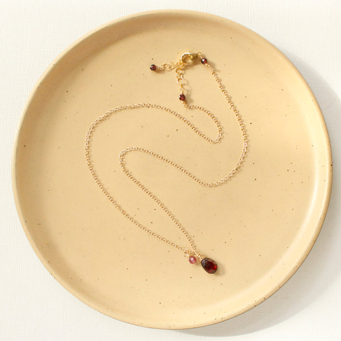 The garnet charm necklace styled on a tan plate to show the adjustable lobster clasp closure