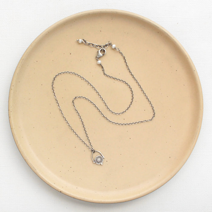 The mini talara shield necklace styled on a tan plate to show the adjustable lobster clasp closure