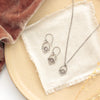 The mini talara shield necklace styled on a tan plate with the matching earrings, linen, orange velvet, and dried grass