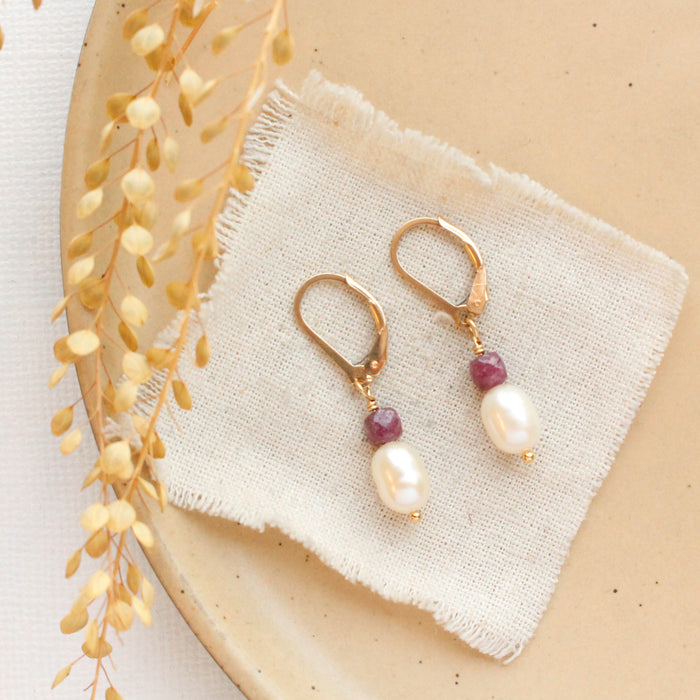 The pearl and ruby gold earrings styled on a tan plate with linen and dried grass