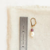 A pearl and ruby gold earring next to a ruler for size reference