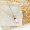 The pearl and ruby gold necklace styled on a tan rock with linen and dried grass