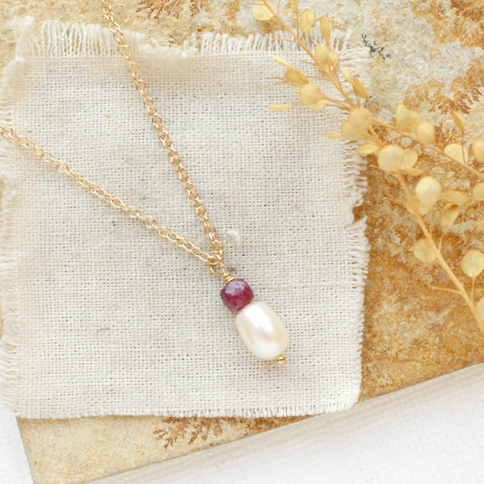 The pearl and ruby gold necklace styled on a tan rock with linen and dried grass