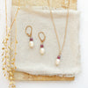 The pearl and ruby gold necklace styled on a tan rock with the matching earrings