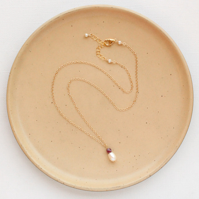 The pearl and ruby gold necklace styled on a tan plate to show the adjustable lobster clasp closure