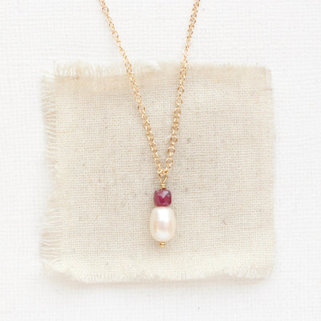 The pearl and ruby gold necklace styled on tan linen