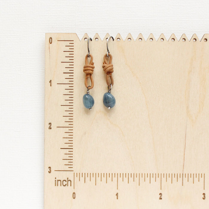 The aquamarine leather earrings styled on a wooden ruler for size reference