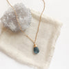 The aquamarine drop necklace styled on tan linen with a gray crystal
