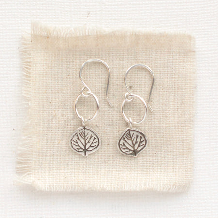 The aspen leaf hoop earrings styled on tan linen