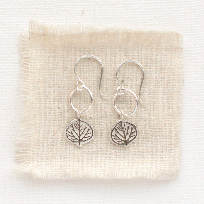 The aspen leaf hoop earrings styled on tan linen