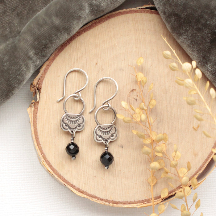 The black tourmaline jolie earrings styled on wood with gray velvet and dried grass