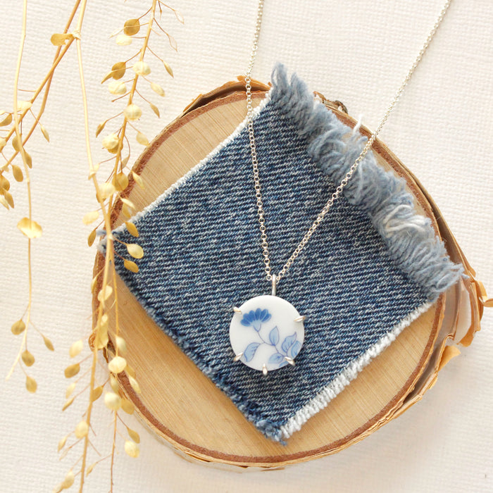 The blue bloom vintage plate necklace styled on wood with blue linen and dried grass