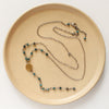 The grandidierite mythos lariat necklace styled on a tan plate to show the adjustable lobster clasp closure