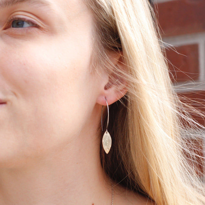 The brass leaf petal earrings being worn by a person