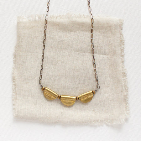 The brass trio mythos necklace styled on tan linen