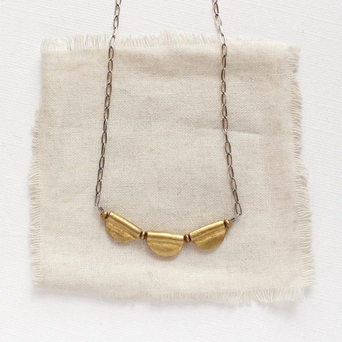 The brass trio mythos necklace styled on tan linen