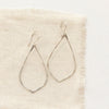 The bright silver pointed hoop earrings styled on tan linen