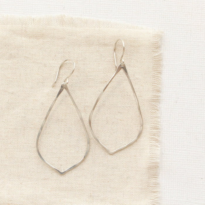 The bright silver pointed hoop earrings styled on tan linen