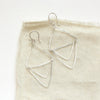 The bright silver triple triangle hoop earrings styled on tan linen