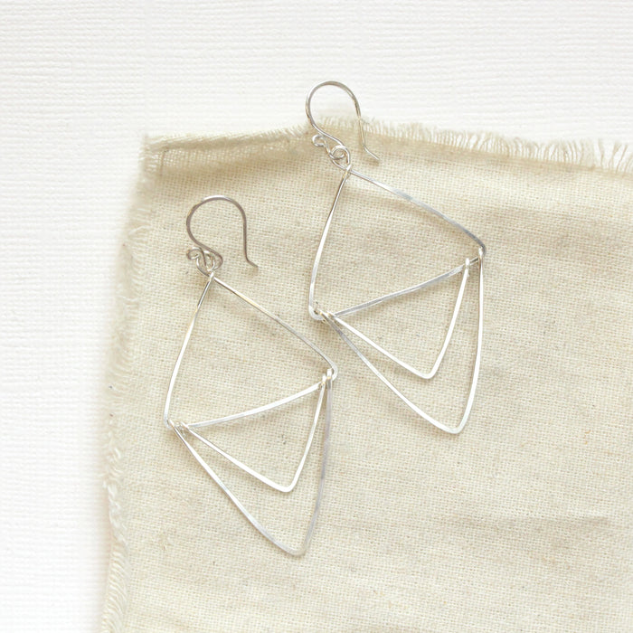 The bright silver triple triangle hoop earrings styled on tan linen