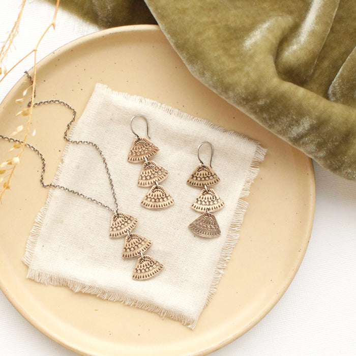 The bronze asmi trio triangle earrings styled on a tan plate with the matching necklace