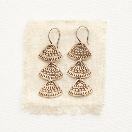 The bronze asmi trio triangle earrings styled on tan linen