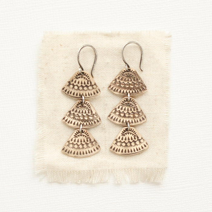 The bronze asmi trio triangle earrings styled on tan linen