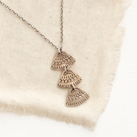 The bronze asmi trio triangle necklace styled on tan linen