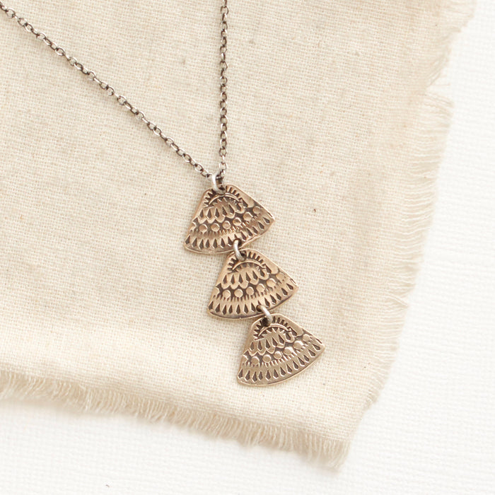 The bronze asmi trio triangle necklace styled on tan linen