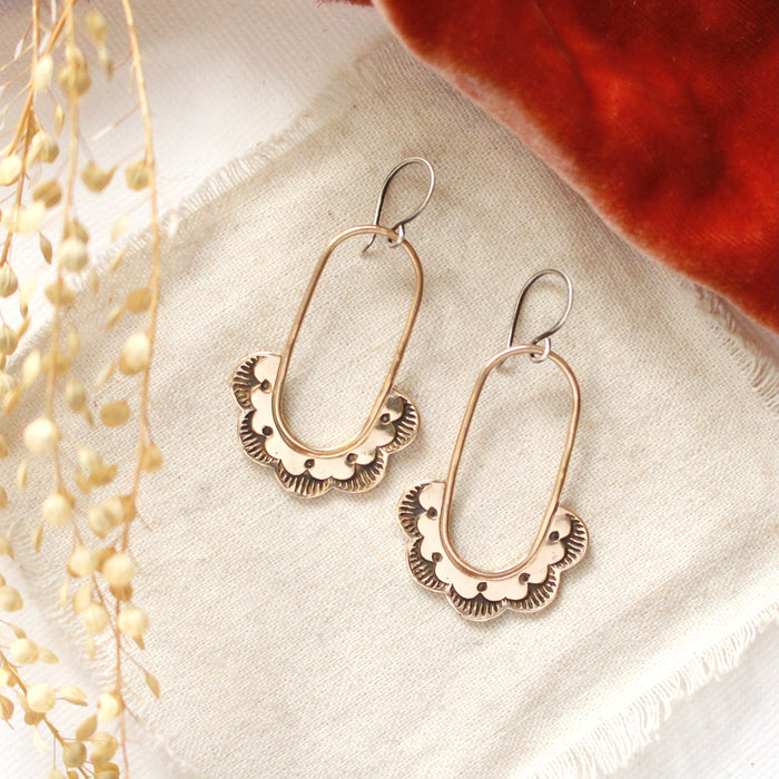 The bronze columbine hoop earrings styled on tan linen with orange velvet and dried grass