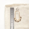 A bronze columbine hoop earring next to a ruler for size reference