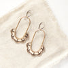 The bronze columbine hoop earrings styled on tan linen 