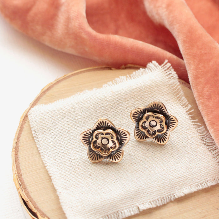 The bronze layered cactus flower post earrings styled on wood with linen and orange velvet