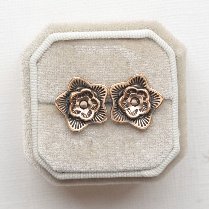 The bronze layered cactus flower post earrings styled on a white velvet box