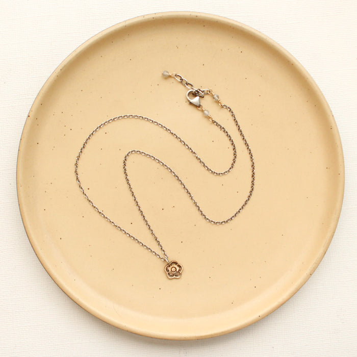 The bronze mini cactus flower necklace styled on a tan plate to show the adjustable lobster clasp closure