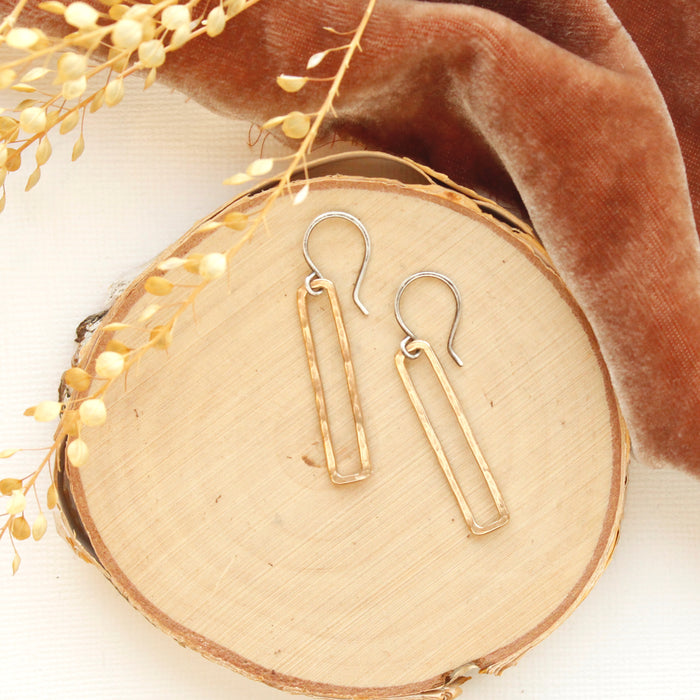 The bronze open bar earrings styled on wood with orange velvet and dried grass