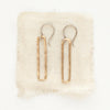 The bronze open bar earrings styled on tan linen