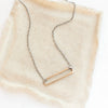 The bronze open bar with silver chain necklace styled on tan linen